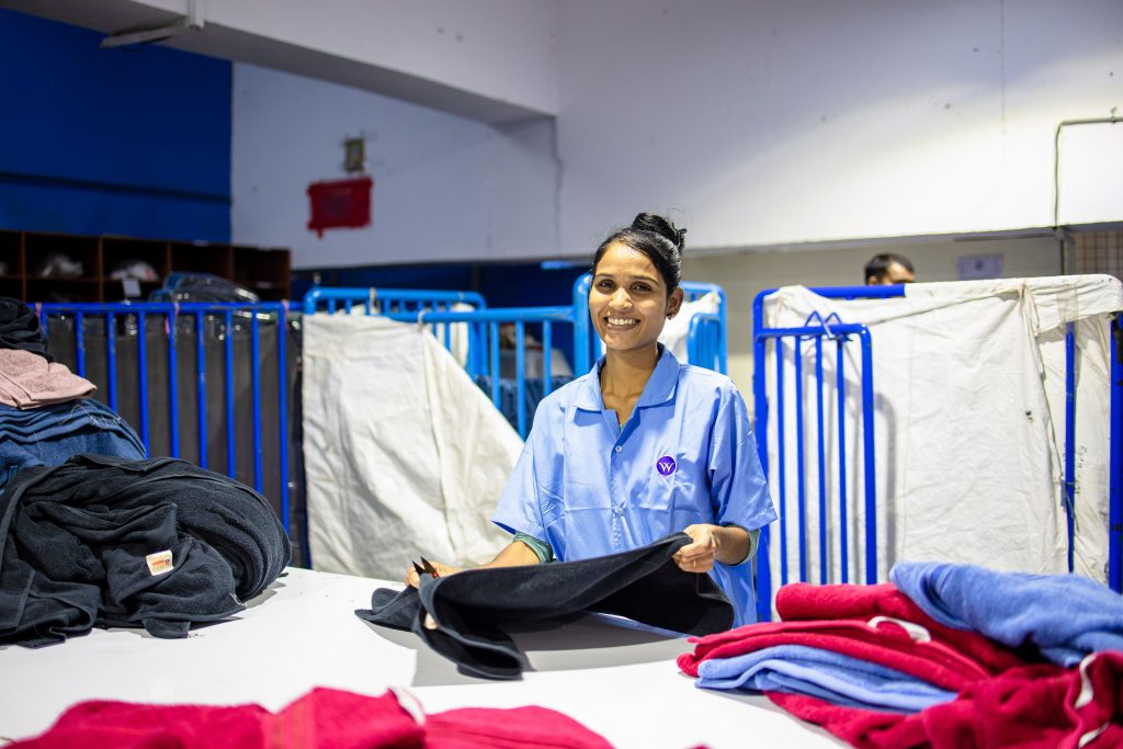 pexels photo 31259218 31259218 A smiling female textile worker folding clothes inside a factory setting, showcasing the blue-collar work environment.