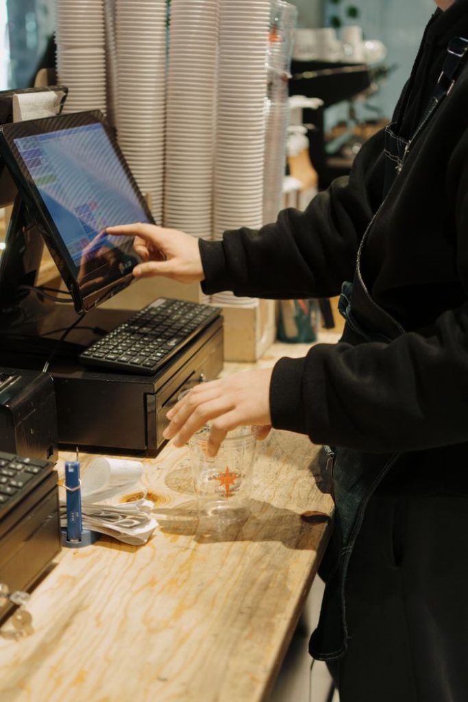 A barista operates a touchscreen register while preparing drink orders at a bustling coffee shop.