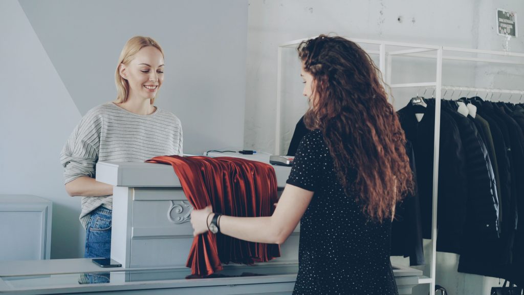 pexels photo 36730430 36730430 Friendly retail interaction between two women at a clothing store counter.
