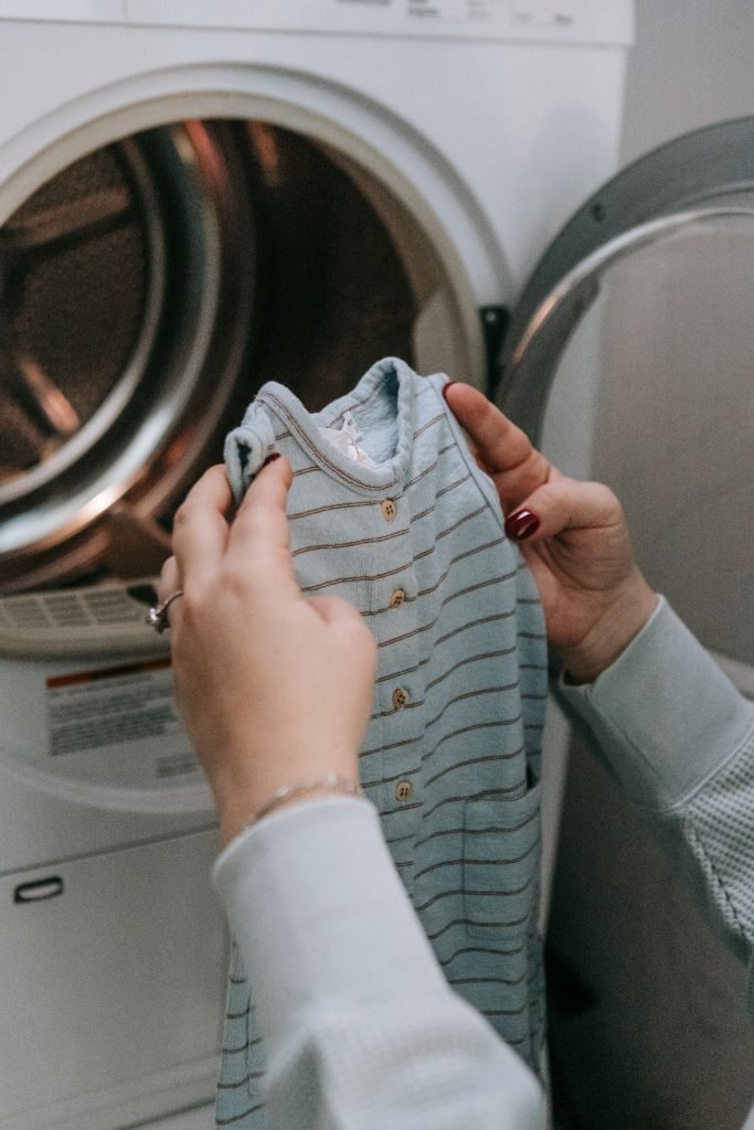 pexels photo 7282794 7282794 A person handles baby clothes next to a front-load washing machine indoors.